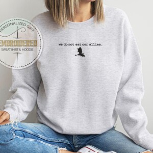 Puede incluir: Una sudadera gris con el texto "we do not eat our allies." y una silueta negra de un drag&oacute;n.