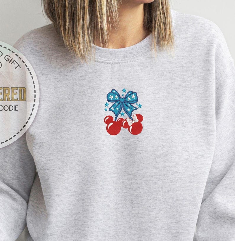 Op de afbeelding: Een lichtgrijs sweatshirt met een patriottisch ontwerp. Het ontwerp toont een blauwe strik met witte sterren en rode Mickey Mouse-vormige kersen. De sweatshirt is een comfortabele, casual stijl.