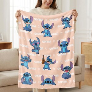 May include: A peach-colored blanket featuring multiple images of the character Stitch in various poses. The word "SOPHIA" is repeated throughout the design, interspersed with heart symbols. The blanket is soft and cozy.