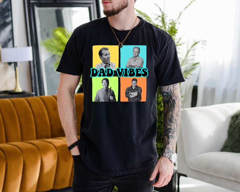 May include: Black t-shirt with the text "DAD VIBES" and four square images of men. The squares are in yellow, blue, green, and orange. The t-shirt is made of a soft material.