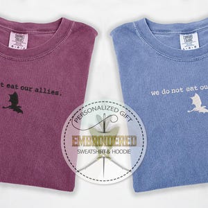May include: Two t-shirts with the text "we do not eat our allies." and a dragon silhouette. The t-shirts are in burgundy and blue.