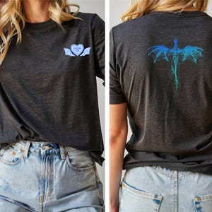 K&ouml;nnte beinhalten: Ein dunkelgraues T-Shirt mit einem blauen und wei&szlig;en Herz-Motiv auf der Vorderseite und einem blauen und gr&uuml;nen Drachen-Motiv auf der R&uuml;ckseite. Das Shirt ist aus einem weichen, bequemen Material.
