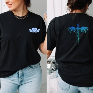 K&ouml;nnte beinhalten: Schwarzes T-Shirt mit einem blauen Herz mit Fl&uuml;geln und dem Text "FOREVER YOURS" auf der Vorderseite und einem blauen Drachen-Design auf der R&uuml;ckseite.