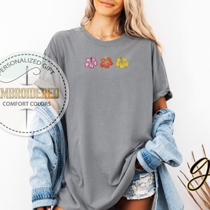 May include: A gray t-shirt with embroidered hibiscus flowers in pink, orange, and yellow. The shirt has the text "EMBROIDERED COMFORT COLORS" in a circular design. The shirt is part of the "Personalized Gift" collection.