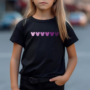 Puede incluir: Una camiseta negra con una fila de cabezas de Mickey Mouse rosas y moradas impresas en la parte delantera.
