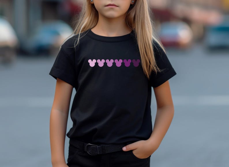 Puede incluir: Una camiseta negra con una fila de cabezas de Mickey Mouse rosas y moradas impresas en la parte delantera.