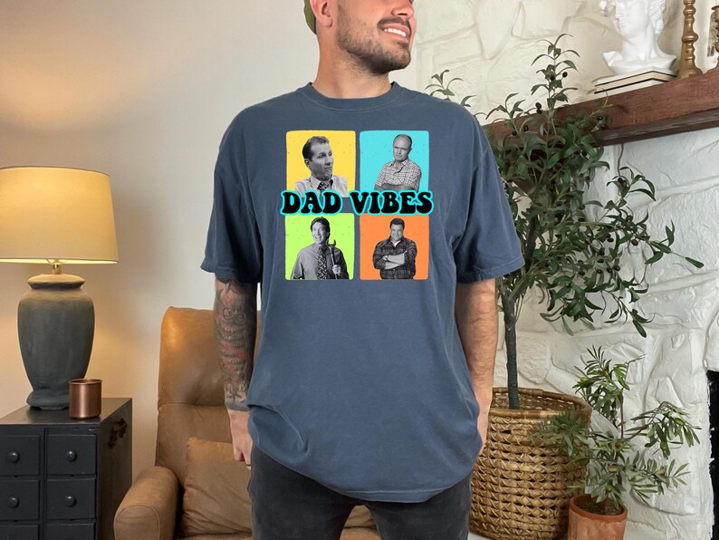 May include: Dark blue t-shirt with a graphic featuring four images of men and the text "DAD VIBES" in a teal font. The shirt is made of a soft material and has short sleeves. The shirt is a comfortable fit.