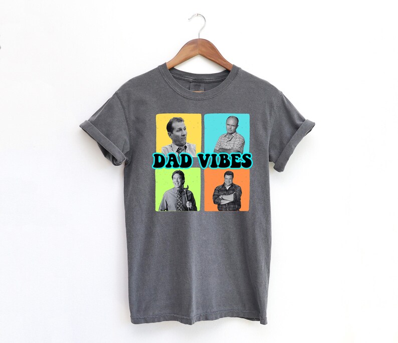 May include: Dark gray t-shirt with the words "DAD VIBES" in teal and black. The shirt features four squares with images of men in each square. The squares are yellow, blue, green, and orange.