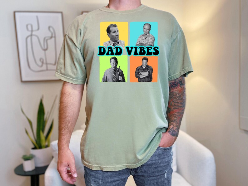 May include: Sage green t-shirt with a graphic that says "DAD VIBES" in black text. The graphic features four squares with images of men in each square. The shirt is made of a soft material.