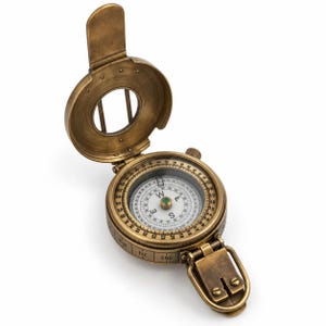 May include: A brass-colored metal compass with a hinged lid and a circular dial featuring cardinal directions and numerical markings. The device includes a small green center point, a folding sight, and a rectangular attachment loop at the base.