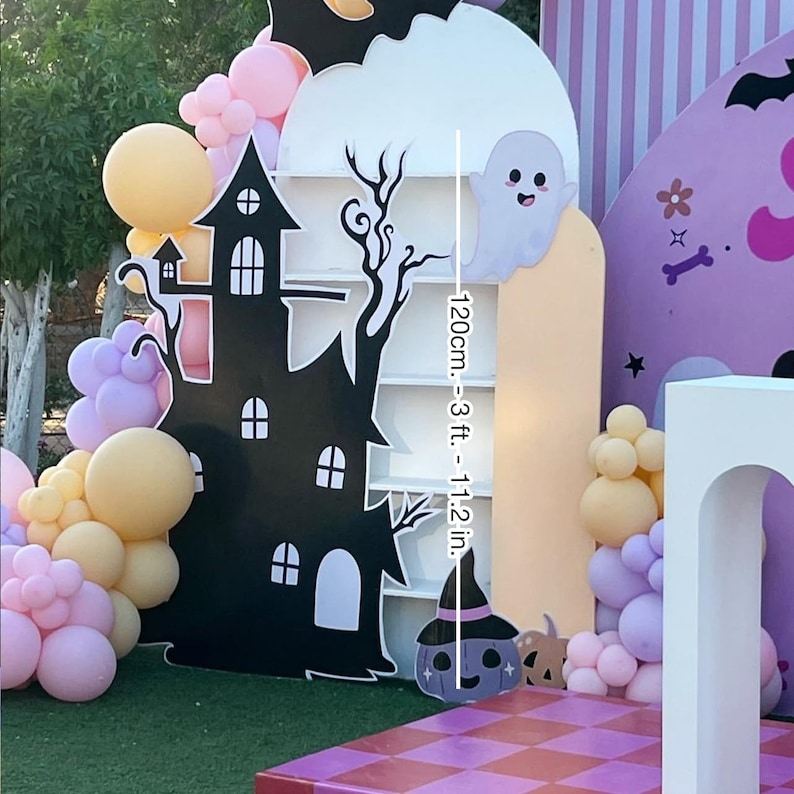 May include: A Halloween-themed party backdrop featuring a black haunted house, a white cloud with a ghost, and a pumpkin with a witch hat. The backdrop is 120cm (3 ft. - 11.2 in.) tall and decorated with balloons in pastel colors.