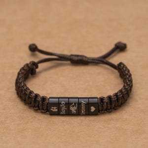 May include: A brown braided bracelet with black beads that have the words "BayJo", "Mommy", and a heart symbol engraved on them.