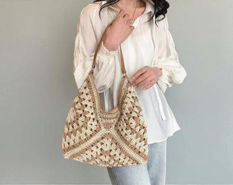 May include: A beige and cream crochet tote bag with brown leather straps. The bag features a geometric pattern and a curved top. The bag is held by a person wearing a white blouse and blue jeans.