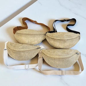 May include: Four beige woven fanny packs are shown. Each has a zip closure and an adjustable strap in brown, black, white, and beige. The bags are made of a woven material, ideal for carrying essentials.