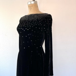 May include: A black velvet dress with a beaded neckline and long sleeves. The dress is fitted and has a straight skirt.