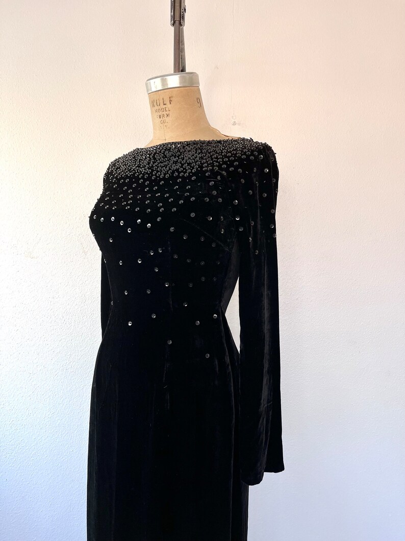 May include: A black velvet dress with a beaded neckline and long sleeves. The dress is fitted and has a straight skirt.