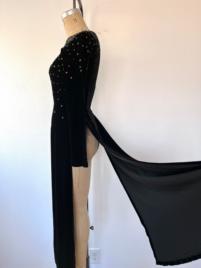 May include: A black velvet gown with a long train and beaded embellishments on the bodice.