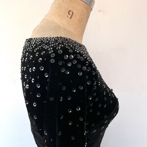 May include: A black velvet dress with a scoop neck and long sleeves. The dress is embellished with sequins.