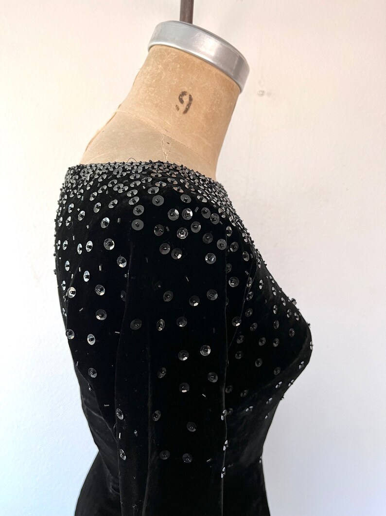 May include: A black velvet dress with a scoop neck and long sleeves. The dress is embellished with sequins.