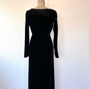 May include: A black velvet dress with a beaded neckline. The dress has long sleeves and a fitted silhouette.