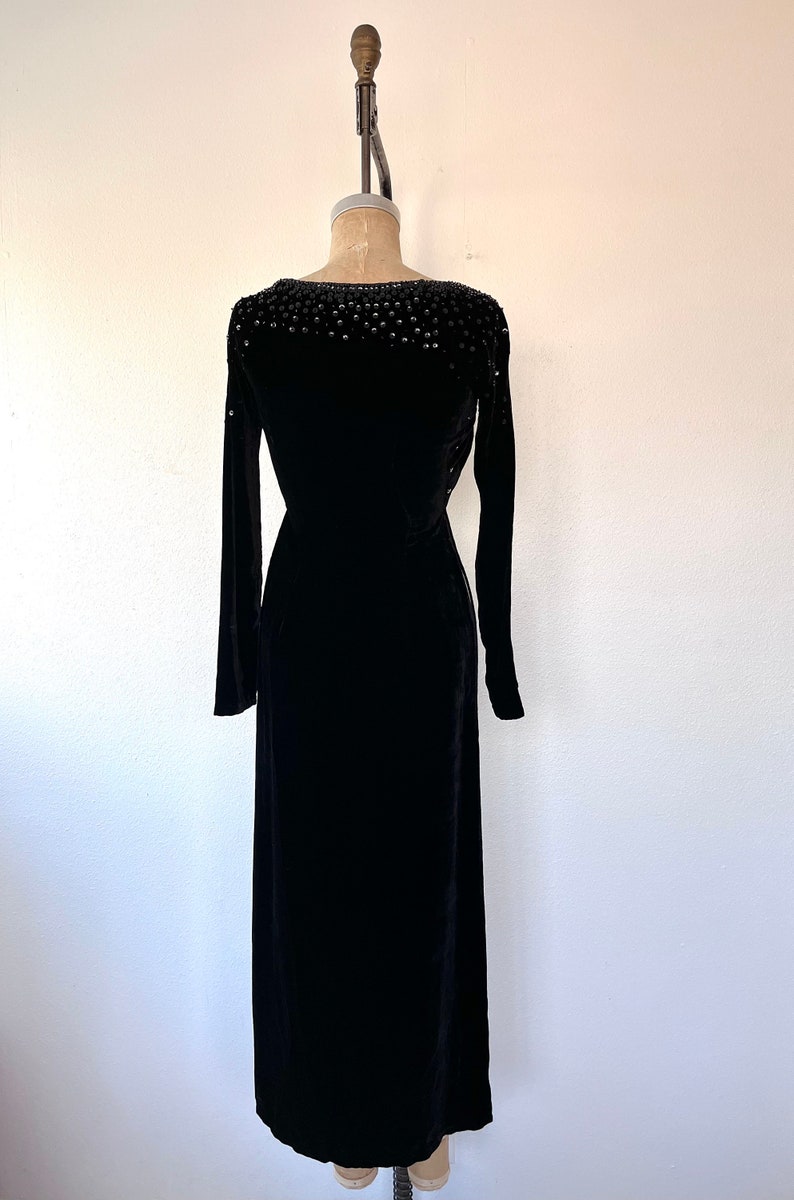 May include: A black velvet dress with a beaded neckline. The dress has long sleeves and a fitted silhouette.