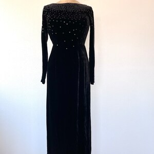 May include: A black velvet gown with a beaded neckline. The gown has long sleeves and a fitted bodice. The skirt is full and flows to the floor.