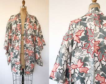 May include: A white kimono with a grey and pink leaf pattern. The kimono is on a mannequin and has long sleeves.