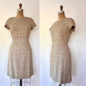 May include: A beige sleeveless dress with a textured woven fabric. The dress has a fitted bodice and a straight skirt.