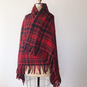 May include: Red and black plaid wool scarf with fringe on the edges. The scarf is draped over a dress form.