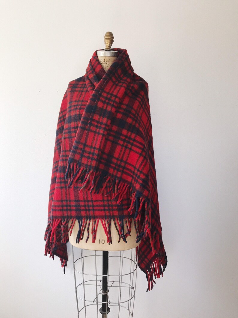 May include: Red and black plaid wool scarf with fringe on the edges. The scarf is draped over a dress form.