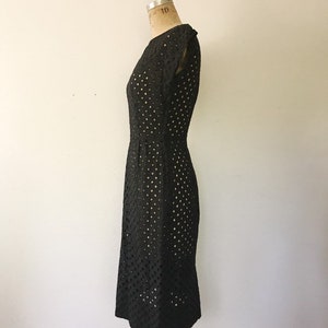 May include: A black sleeveless dress with a round neckline and a dotted pattern. The dress is fitted and has a knee-length hem.
