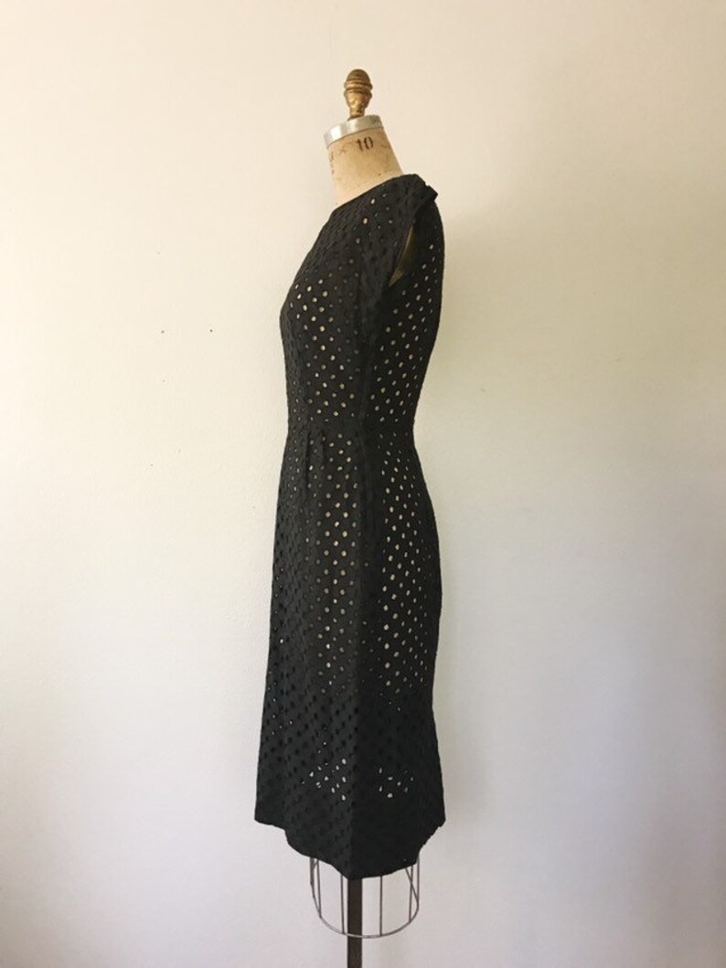 May include: A black sleeveless dress with a round neckline and a dotted pattern. The dress is fitted and has a knee-length hem.