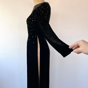 May include: A long black velvet dress with a beaded neckline and side slits. The dress is on a white background.
