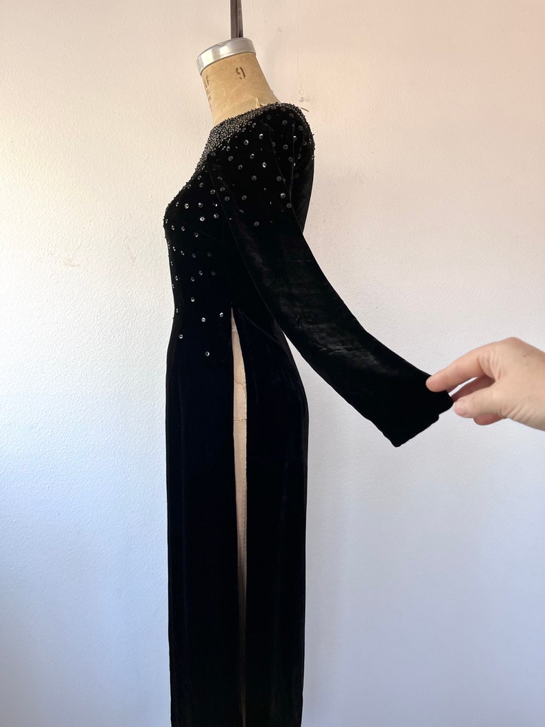 May include: A long black velvet dress with a beaded neckline and side slits. The dress is on a white background.