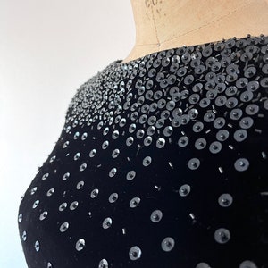May include: Black velvet top with a scattered pattern of silver sequins. The sequins are larger near the neckline and gradually decrease in size towards the bottom of the image.