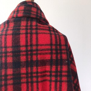 May include: Red and black plaid wool blanket with a frayed edge. The blanket is folded and draped over a wooden mannequin.