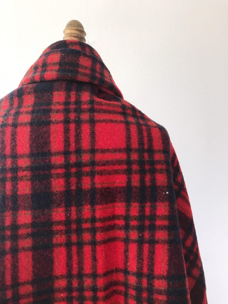 May include: Red and black plaid wool blanket with a frayed edge. The blanket is folded and draped over a wooden mannequin.