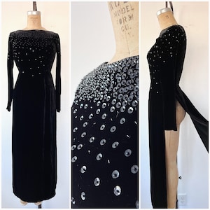 May include: A long black velvet gown with a high neckline and long sleeves. The gown is embellished with silver sequins in a graduated pattern.