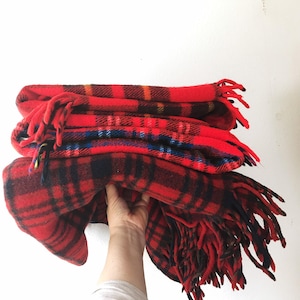 Puede incluir: Una pila de mantas de franela roja y negra a cuadros con flecos. Las mantas están dobladas y apiladas una encima de la otra.