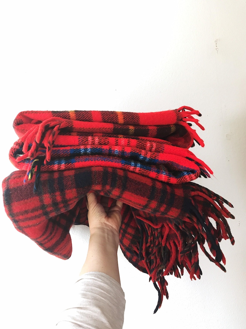May include: A stack of red and black plaid fleece blankets with fringe. The blankets are folded and stacked on top of each other.