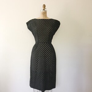 May include: A black, sleeveless dress with a fitted silhouette and a delicate eyelet pattern. The dress has a round neckline and a slightly flared skirt.