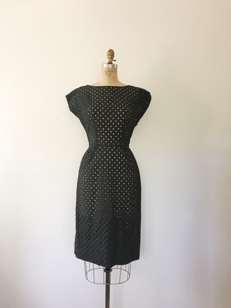 May include: A black, sleeveless dress with a fitted silhouette and a delicate eyelet pattern. The dress has a round neckline and a slightly flared skirt.