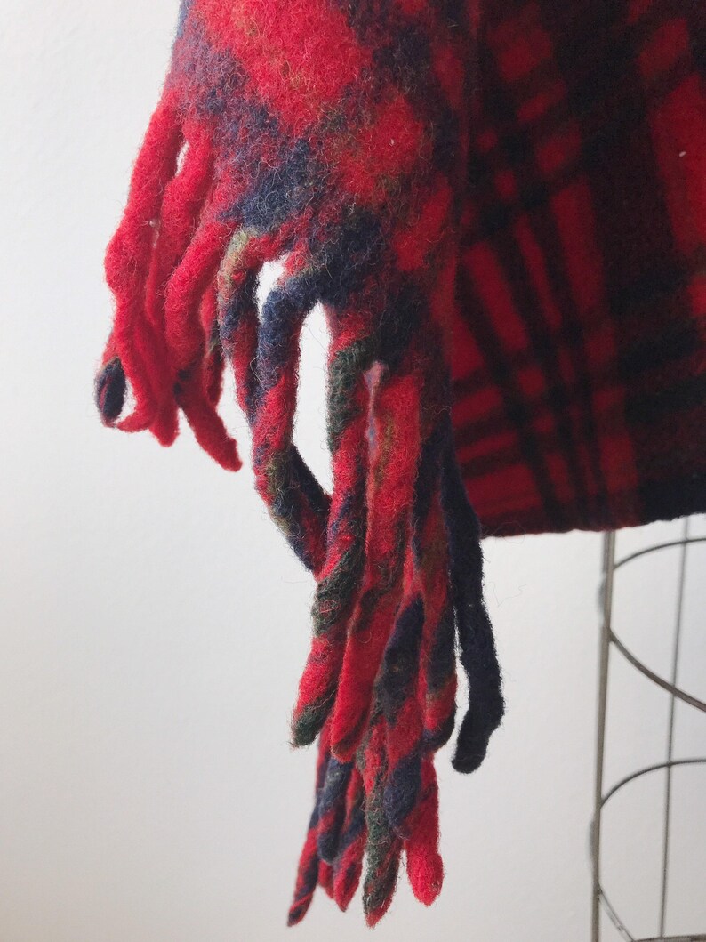 May include: Red and black plaid scarf with long fringe tassels. The scarf is made of a soft, fuzzy material.