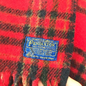 May include: Red and black plaid Pendleton wool blanket with fringe. The label reads "Pendleton Woolen Mills, Portland, Oregon, 100% Virgin Wool, Pure Virgin Wool."