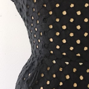 May include: Black dress with a geometric pattern of cut-out circles. The dress is fitted and has a flared skirt.