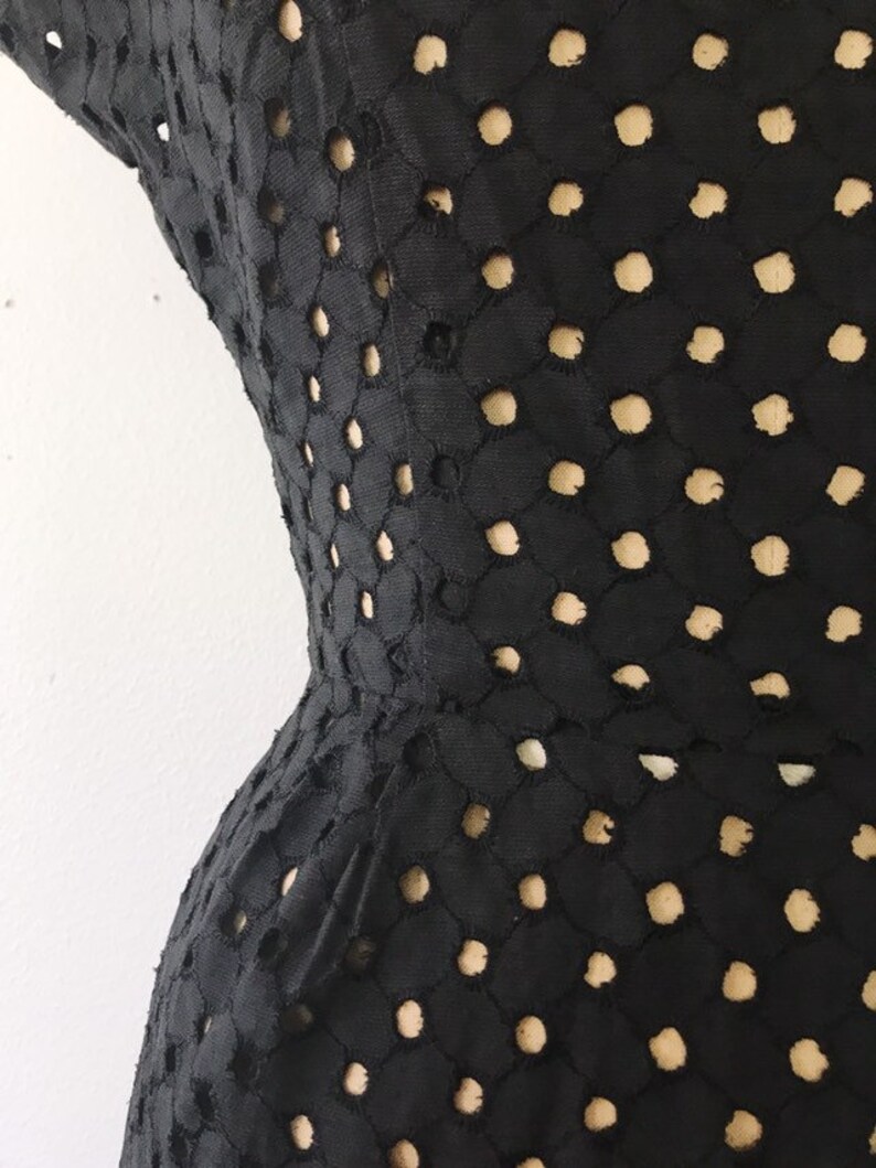 May include: Black dress with a geometric pattern of cut-out circles. The dress is fitted and has a flared skirt.
