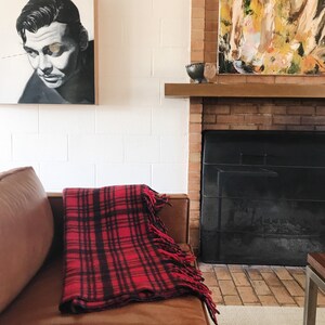 May include: A red and black plaid throw blanket with fringe on a brown leather couch in front of a brick fireplace.
