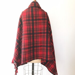 May include: Red and black plaid wool blanket with fringe. The blanket is draped over a mannequin.