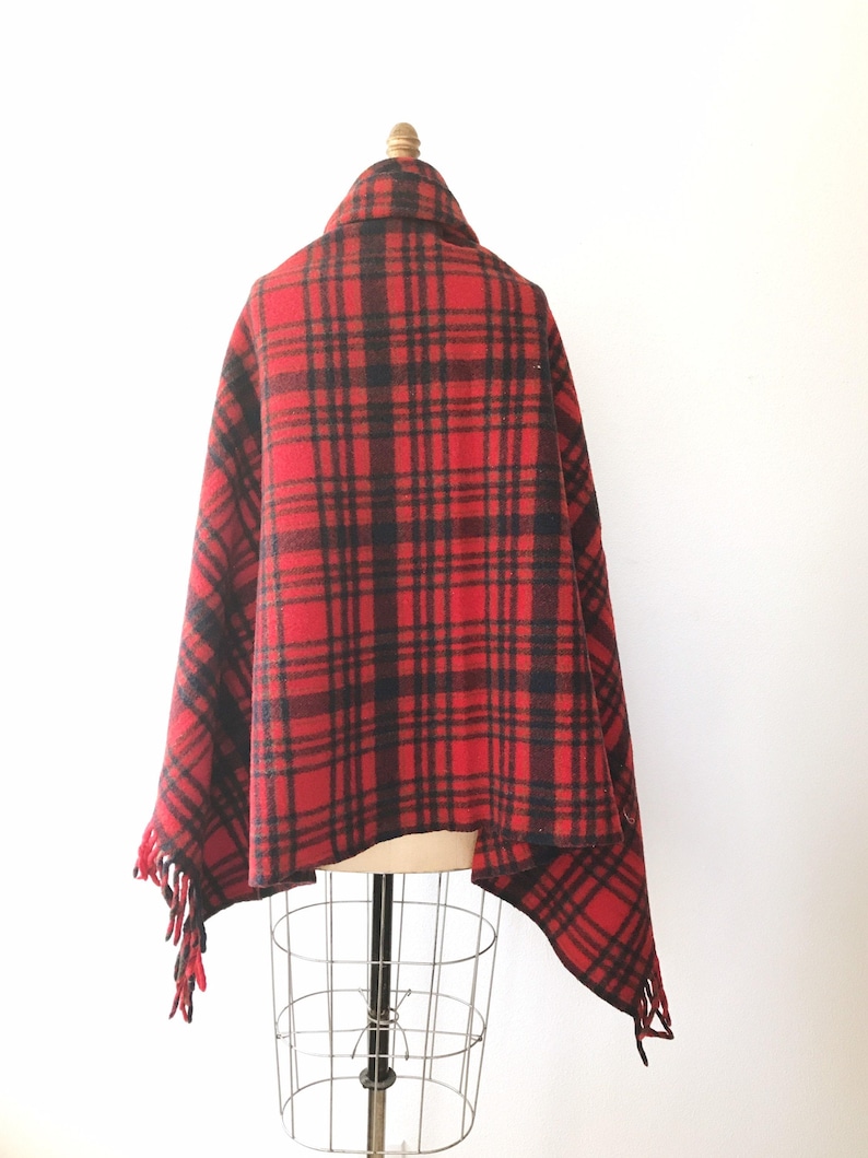 May include: Red and black plaid wool blanket with fringe. The blanket is draped over a mannequin.