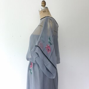 Op de afbeelding: Een lichtblauwe, doorschijnende jurk met een bloemenprint en zwarte bies. De jurk heeft een losse, vloeiende silhouet en een ronde halslijn.